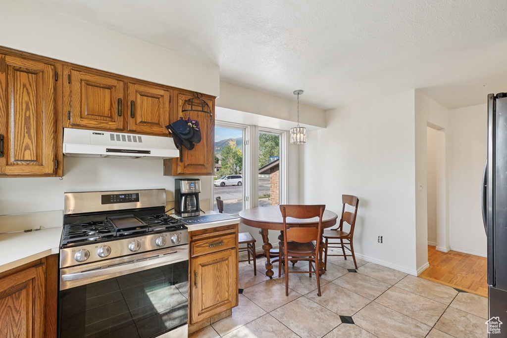Kitchen featuring appliances with stainless steel finishes, under cabinet range hood, brown cabinetry, light countertops, and a textured ceiling