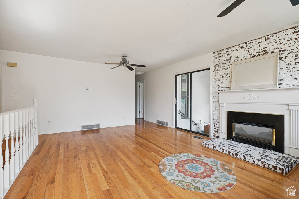 Unfurnished living room with a ceiling fan, wood finished floors, and a glass covered fireplace