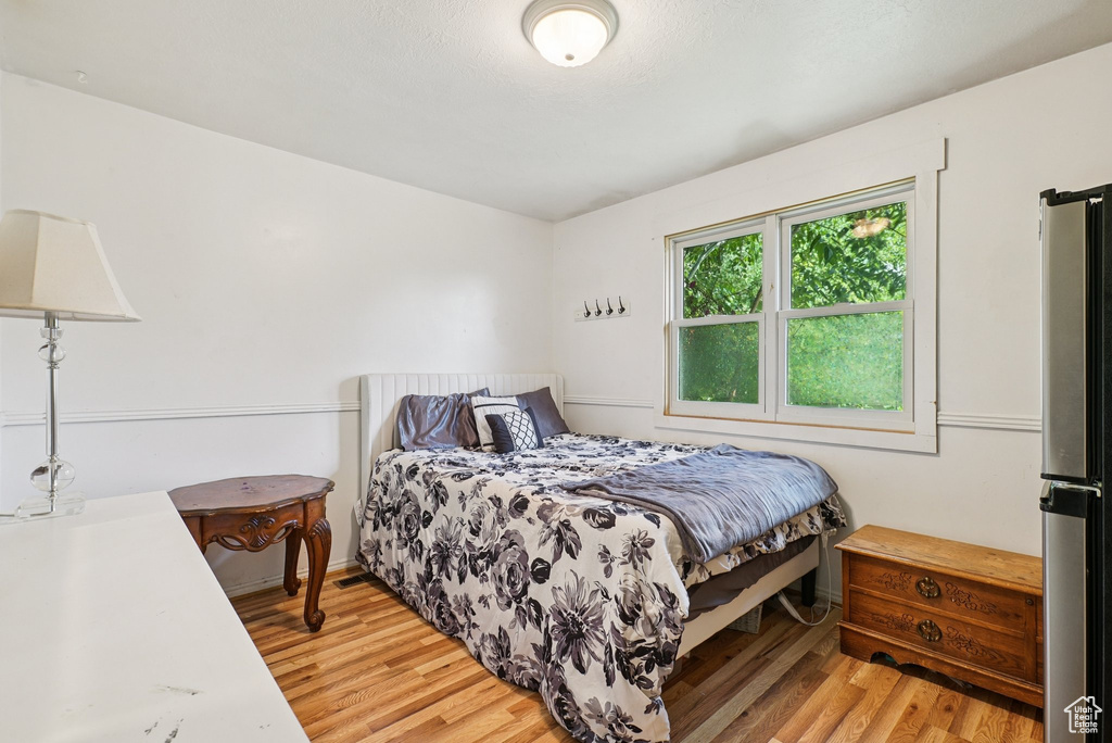 Bedroom with light wood finished floors and freestanding refrigerator