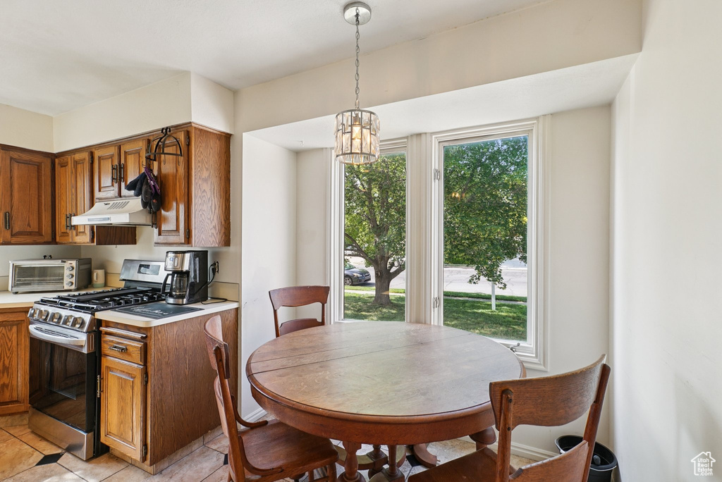 Kitchen featuring stainless steel gas range oven, under cabinet range hood, brown cabinetry, light countertops, and a chandelier