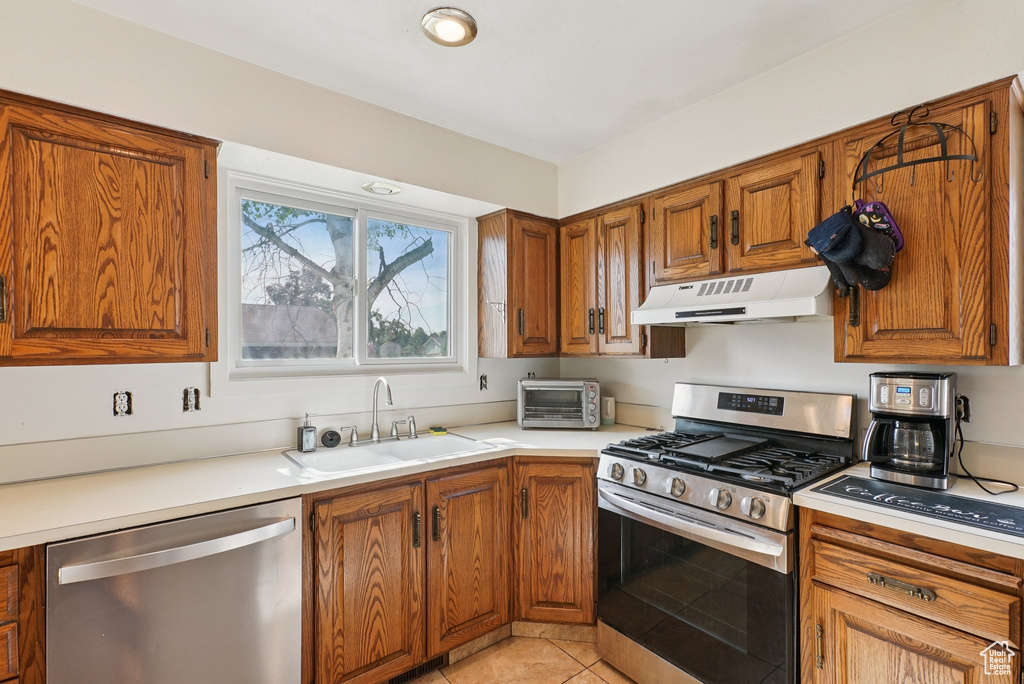 Kitchen featuring stainless steel appliances, under cabinet range hood, a sink, and brown cabinetry