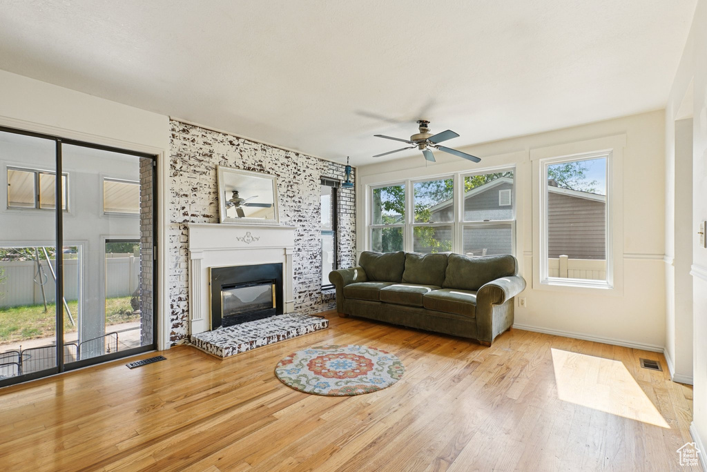 Living area with a ceiling fan, wood finished floors, baseboards, and a glass covered fireplace
