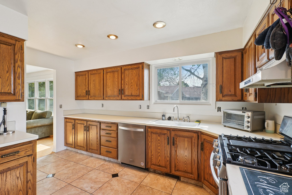 Kitchen with appliances with stainless steel finishes, a sink, brown cabinetry, light countertops, and light tile patterned floors
