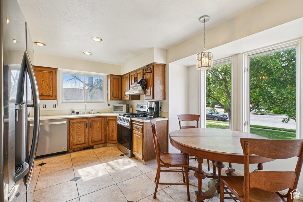 Kitchen with stainless steel appliances, brown cabinets, a sink, light countertops, and under cabinet range hood