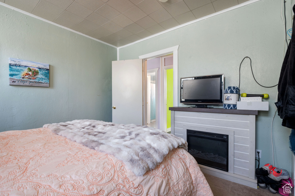 Bedroom with crown molding, a glass covered fireplace, and carpet flooring