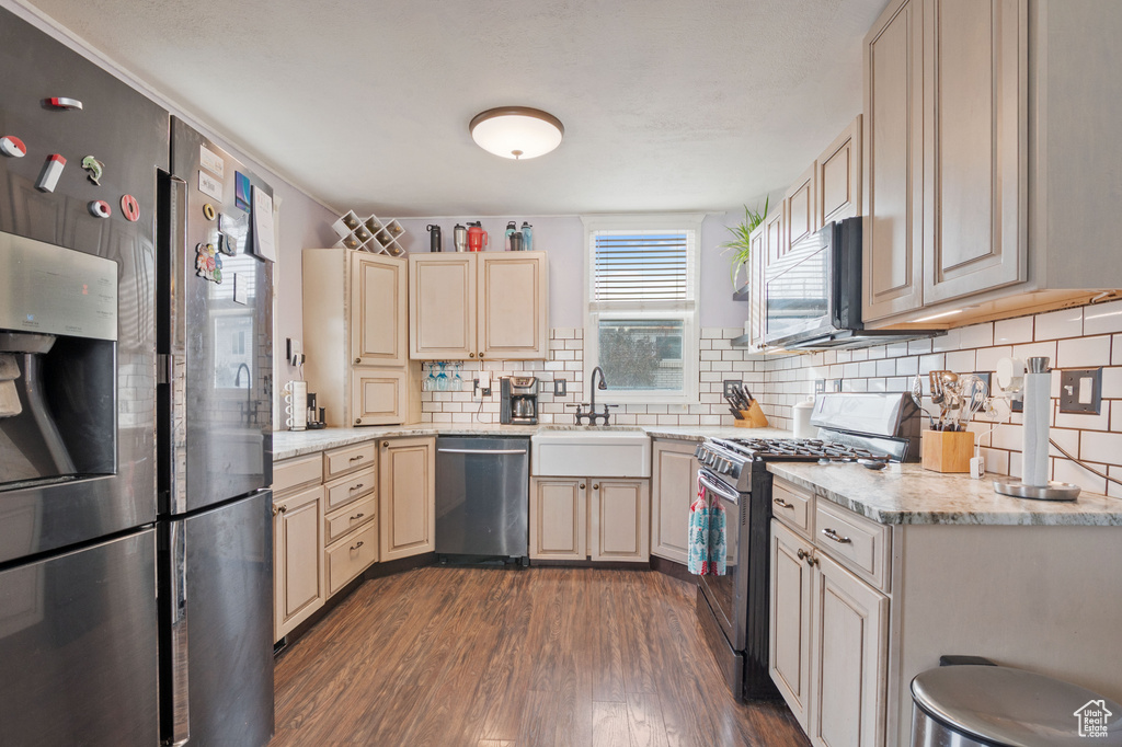 Kitchen featuring appliances with stainless steel finishes, a sink, dark wood-type flooring, decorative backsplash, and light stone counters