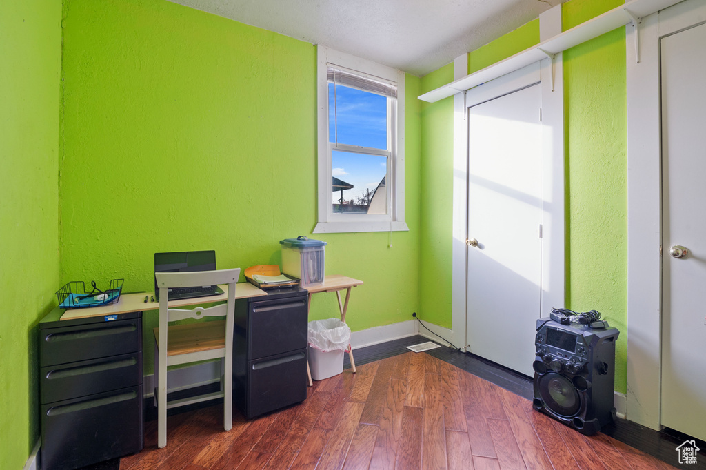 Home office with a textured wall, dark wood-type flooring, and baseboards