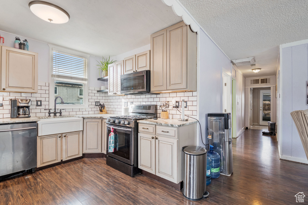 Kitchen featuring appliances with stainless steel finishes, dark wood-style flooring, cream cabinetry, and a textured ceiling