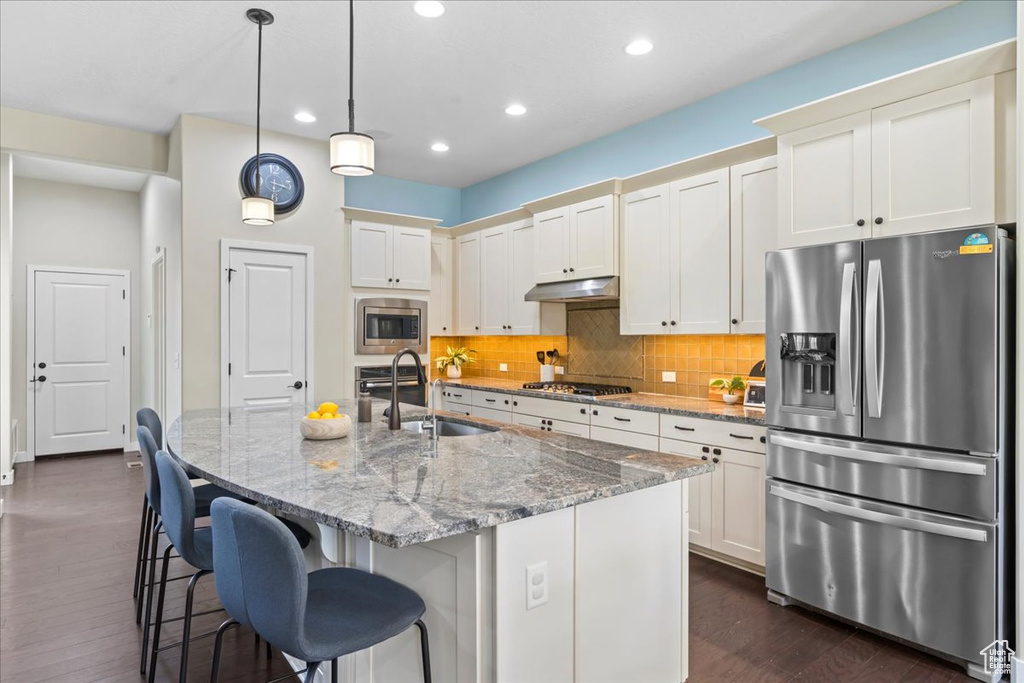 Kitchen with appliances with stainless steel finishes, dark wood finished floors, tasteful backsplash, recessed lighting, and a kitchen bar