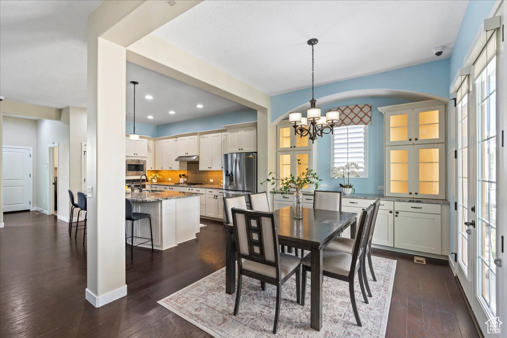 Dining space with a chandelier, healthy amount of natural light, dark wood-style flooring, baseboards, and recessed lighting