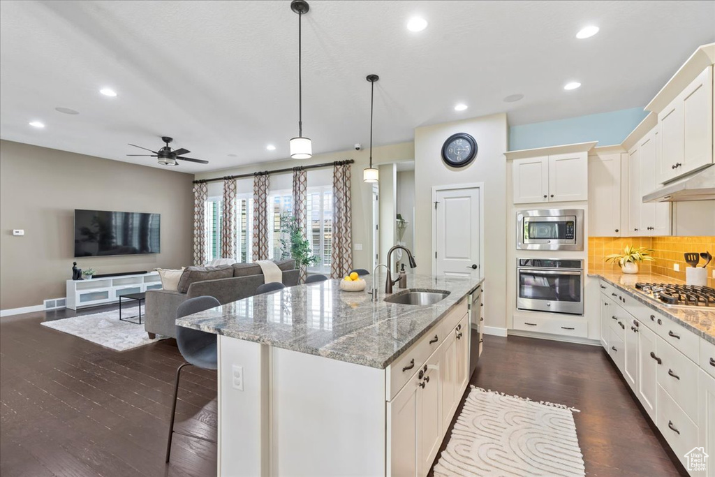Kitchen featuring stainless steel appliances, a sink, baseboards, tasteful backsplash, and dark wood-style floors