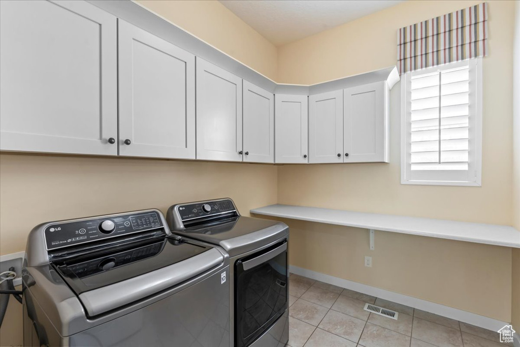Washroom with cabinet space, independent washer and dryer, light tile patterned flooring, and baseboards