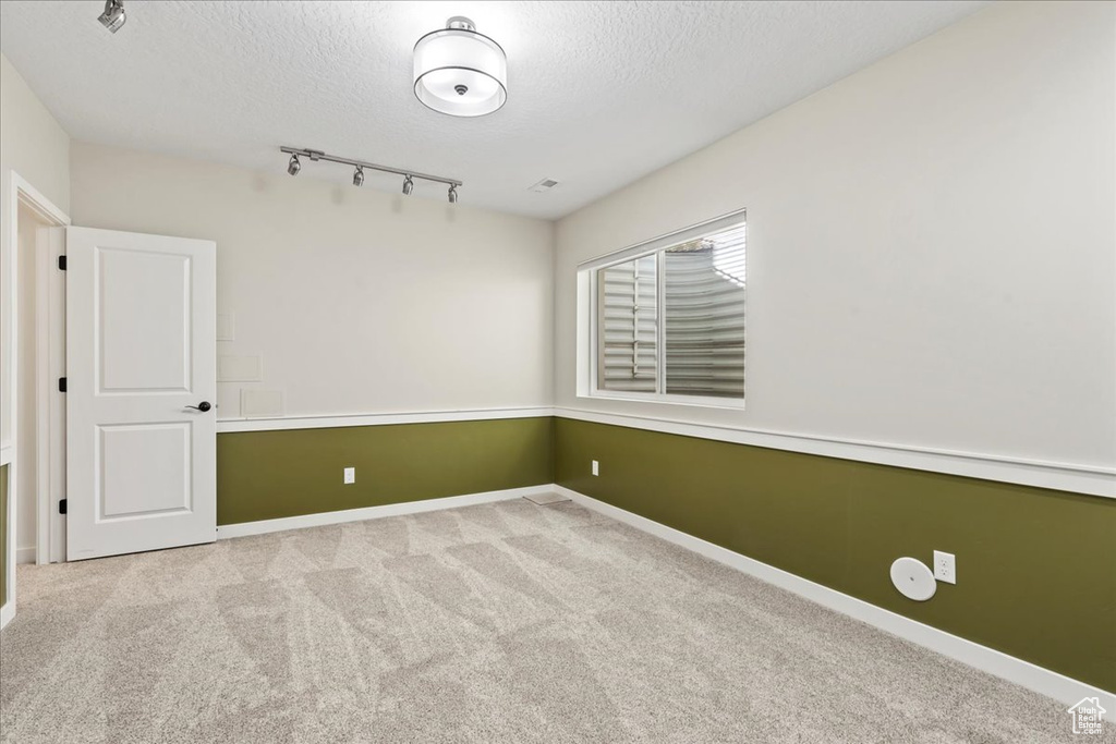 Carpeted empty room with a textured ceiling, rail lighting, and baseboards