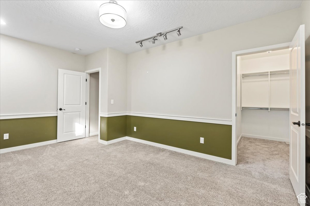 Unfurnished bedroom with a textured ceiling, carpet, a spacious closet, and baseboards