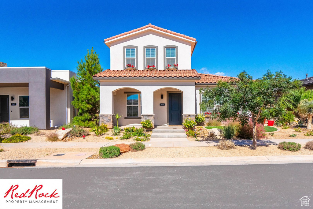 Mediterranean / spanish-style house featuring stucco siding, a tile roof, a porch, and stone siding