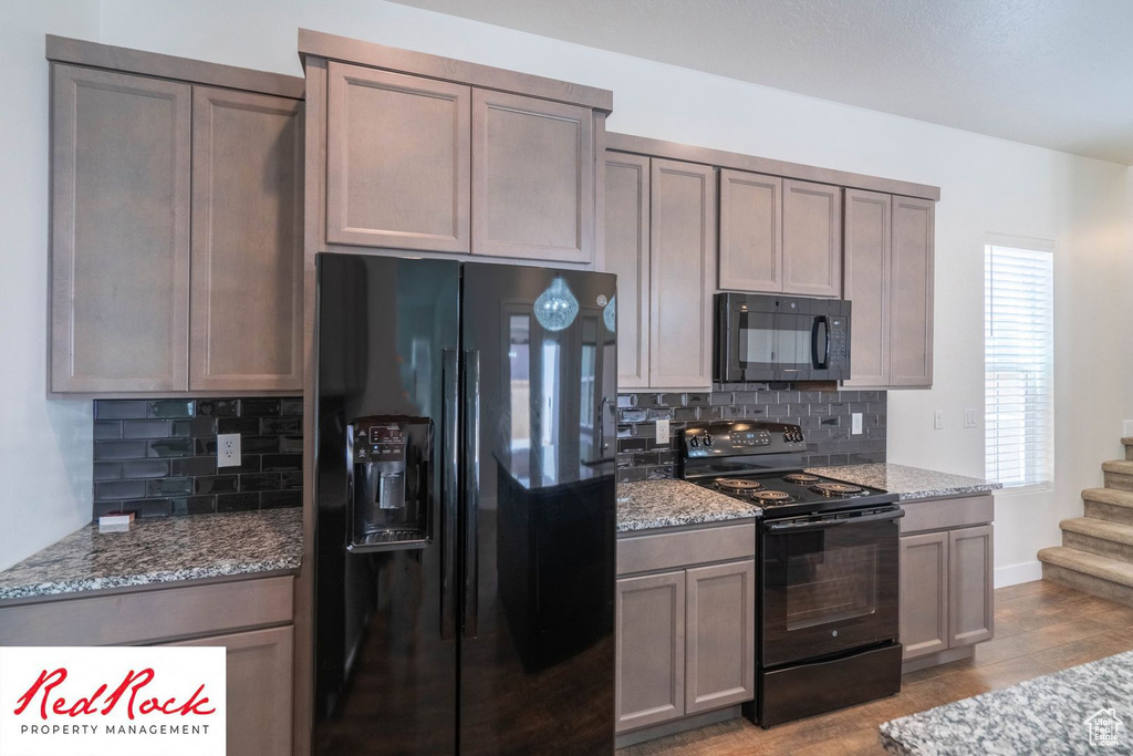 Kitchen with black appliances, decorative backsplash, and light stone counters