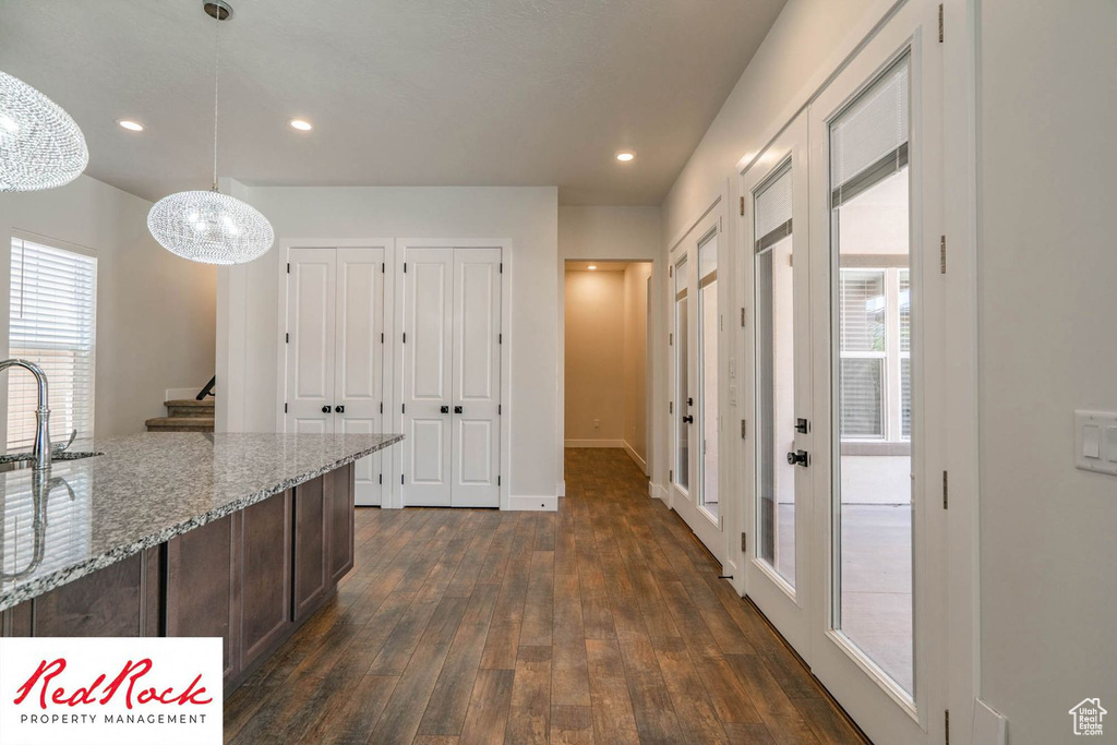Kitchen featuring a chandelier, dark wood finished floors, a sink, dark brown cabinetry, and light stone countertops