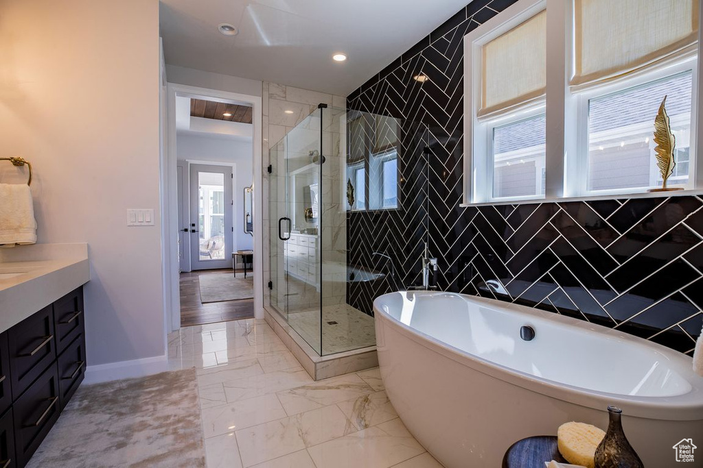 Bathroom featuring vanity, a stall shower, a freestanding bath, marble look tiles, and baseboards
