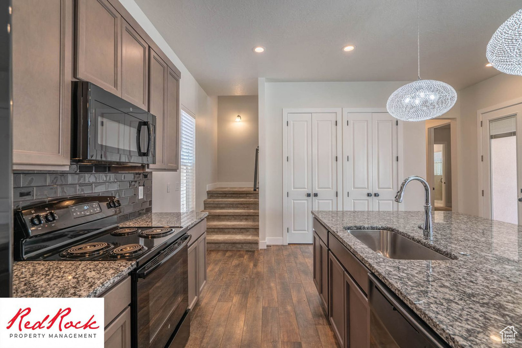 Kitchen featuring black appliances, a sink, dark wood-style flooring, dark stone counters, and recessed lighting