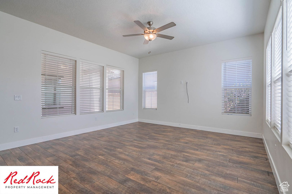 Empty room with a ceiling fan, dark wood-style floors, and baseboards