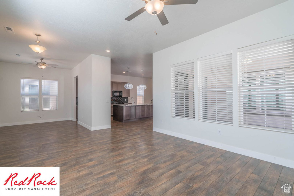 Unfurnished living room featuring ceiling fan, dark wood-style floors, baseboards, recessed lighting, and a sink