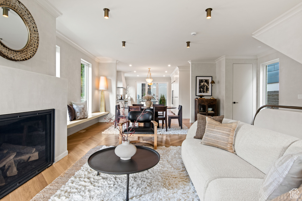 Living area with plenty of natural light, recessed lighting, light wood finished floors, crown molding, and a glass covered fireplace
