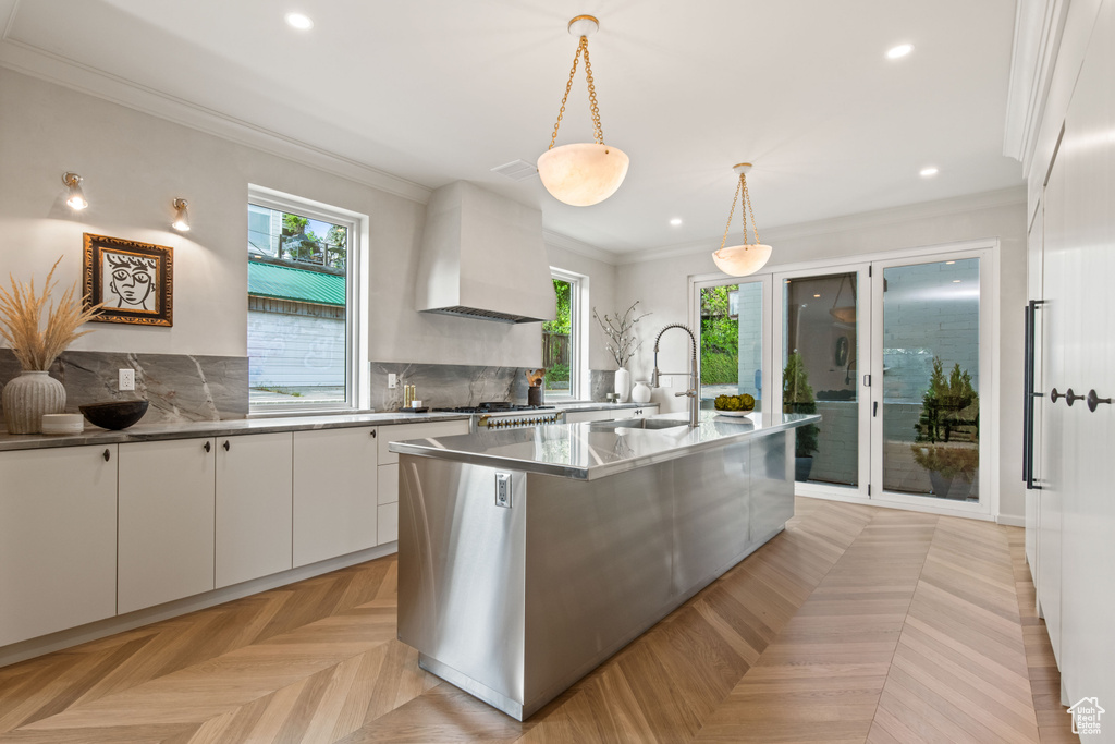 Kitchen featuring a sink, custom range hood, plenty of natural light, white cabinets, and ornamental molding