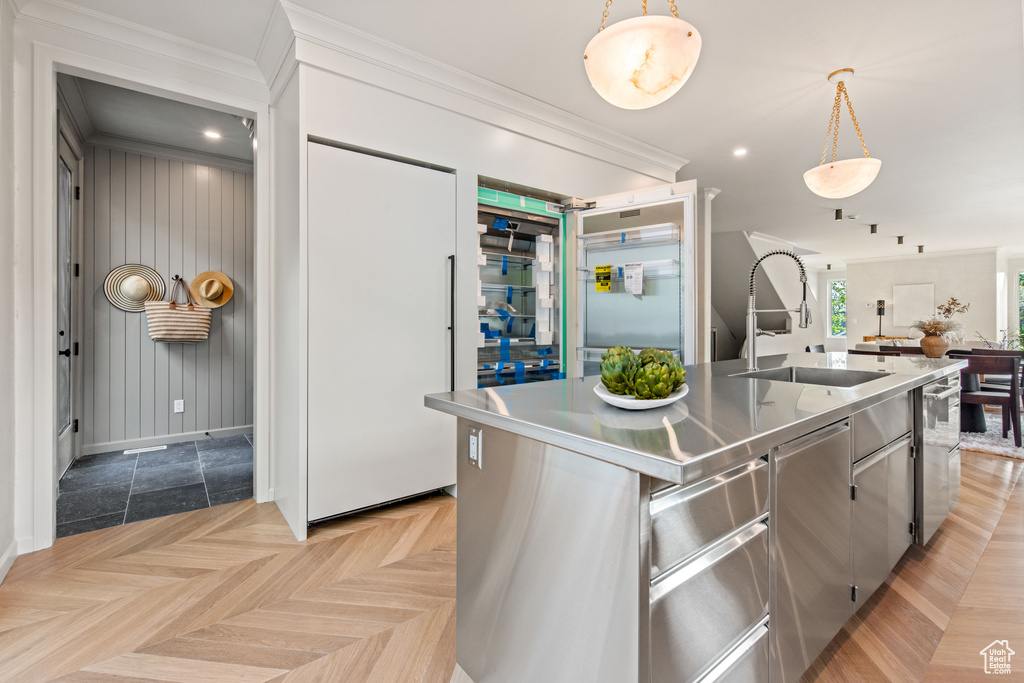 Kitchen with stainless steel countertops, a sink, hanging light fixtures, baseboards, and a kitchen island with sink