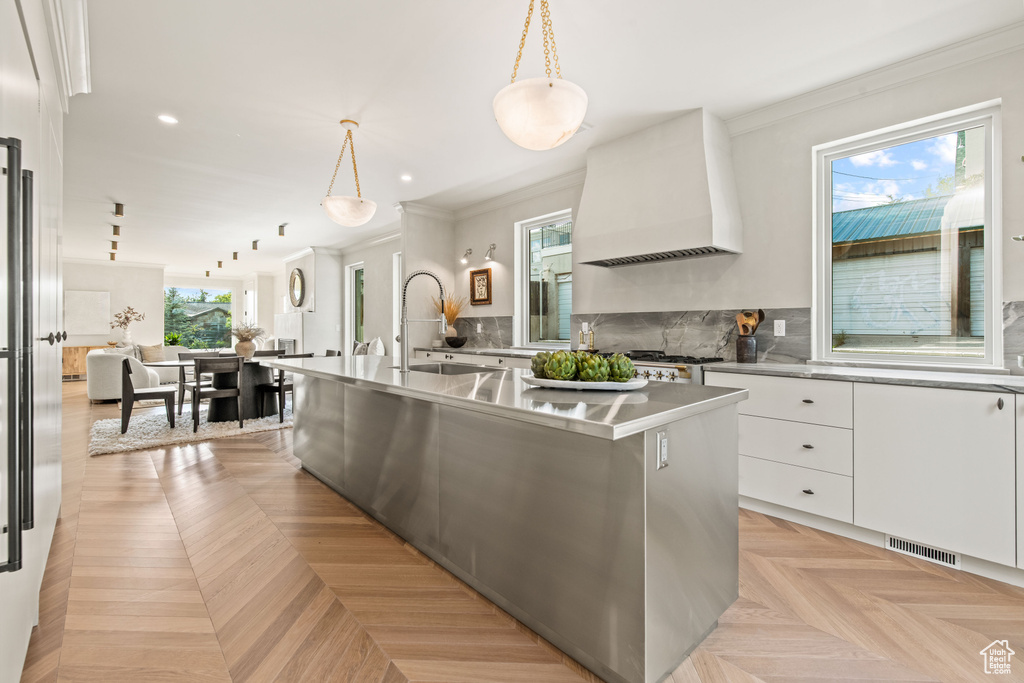 Kitchen with custom range hood, modern cabinets, white cabinetry, crown molding, and stainless steel counters