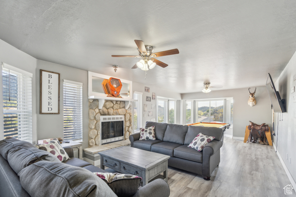 Living area featuring a ceiling fan, light wood-style flooring, a fireplace, baseboards, and a textured ceiling