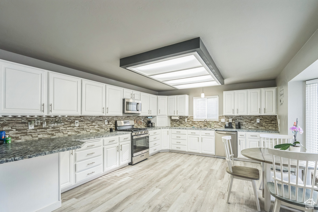 Kitchen with appliances with stainless steel finishes, a sink, decorative backsplash, light wood-style flooring, and white cabinetry