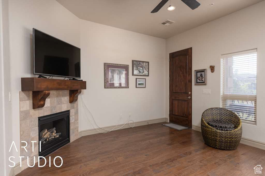 Living room with wood finished floors, a ceiling fan, a tile fireplace, and baseboards
