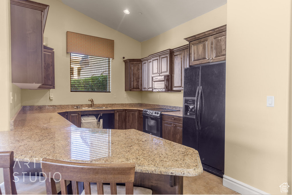 Kitchen featuring black appliances, a peninsula, dark brown cabinetry, vaulted ceiling, and a kitchen breakfast bar