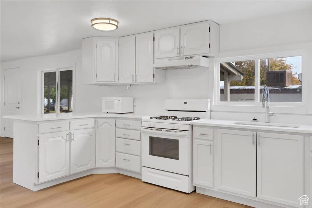Kitchen featuring white appliances, a sink, a peninsula, under cabinet range hood, and white cabinets