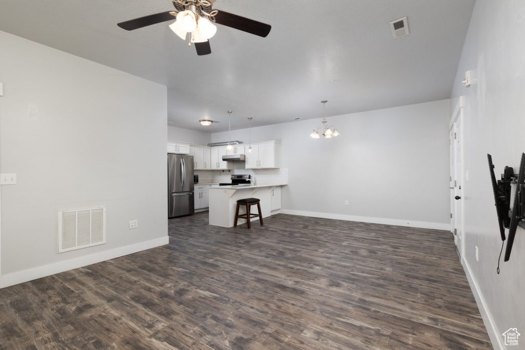 Unfurnished living room with ceiling fan, dark wood-style flooring, a chandelier, and baseboards