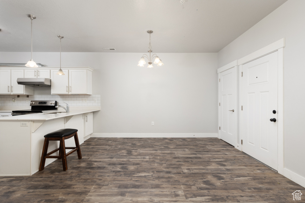 Kitchen featuring stainless steel range with electric cooktop, under cabinet range hood, a chandelier, a breakfast bar area, and light countertops