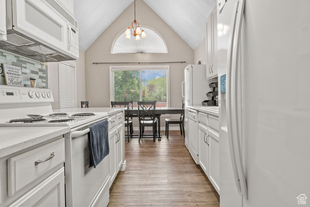 Kitchen featuring white appliances, light wood-type flooring, white cabinets, a chandelier, and hanging light fixtures