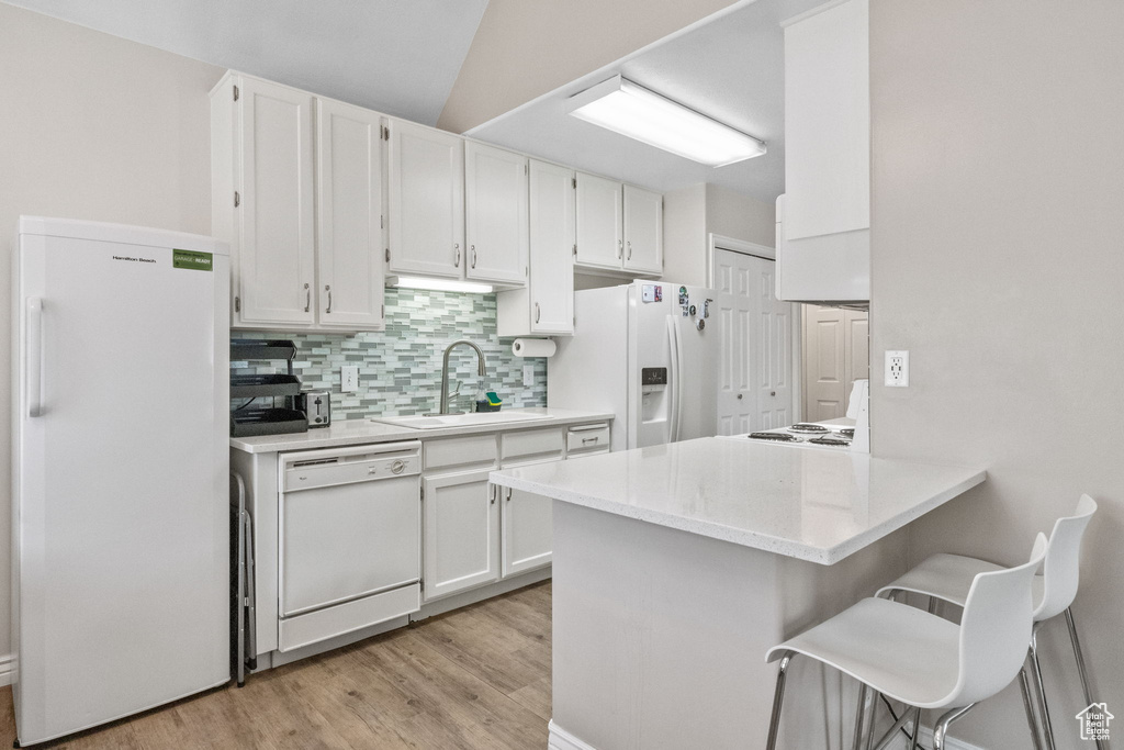 Kitchen with white appliances, a sink, white cabinets, tasteful backsplash, and lofted ceiling