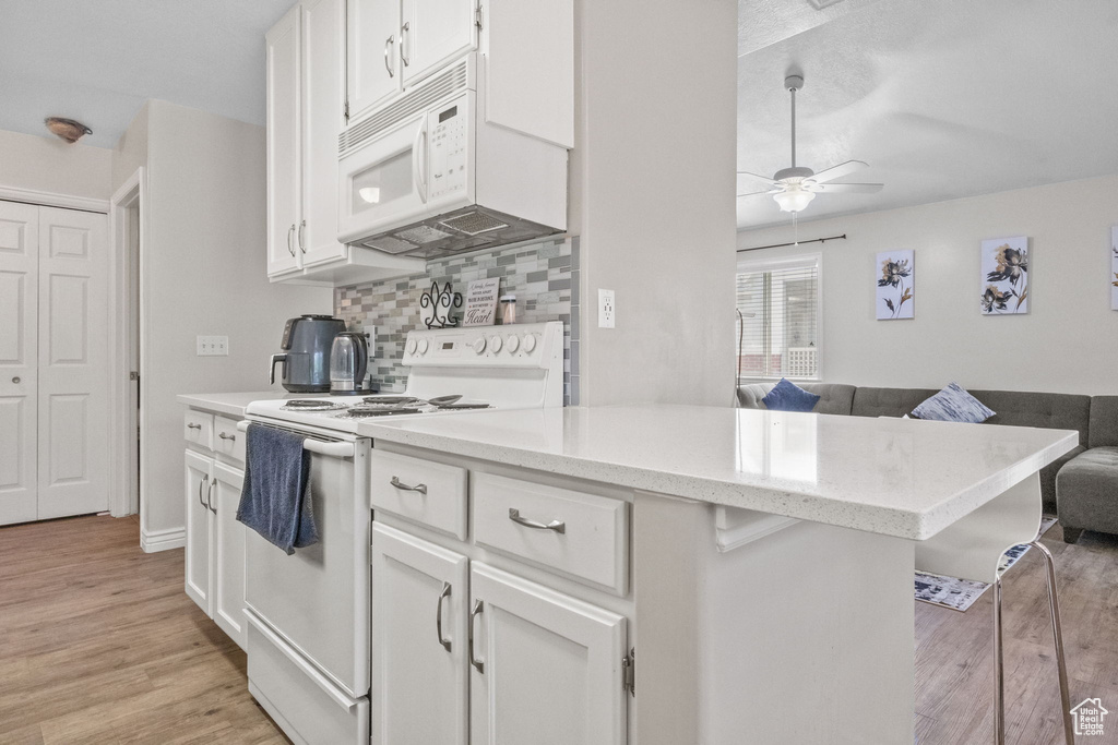 Kitchen featuring white appliances, open floor plan, ceiling fan, white cabinets, and light wood-type flooring