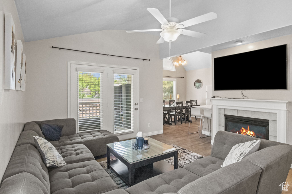 Living room with vaulted ceiling, light wood-type flooring, ceiling fan, a tiled fireplace, and baseboards