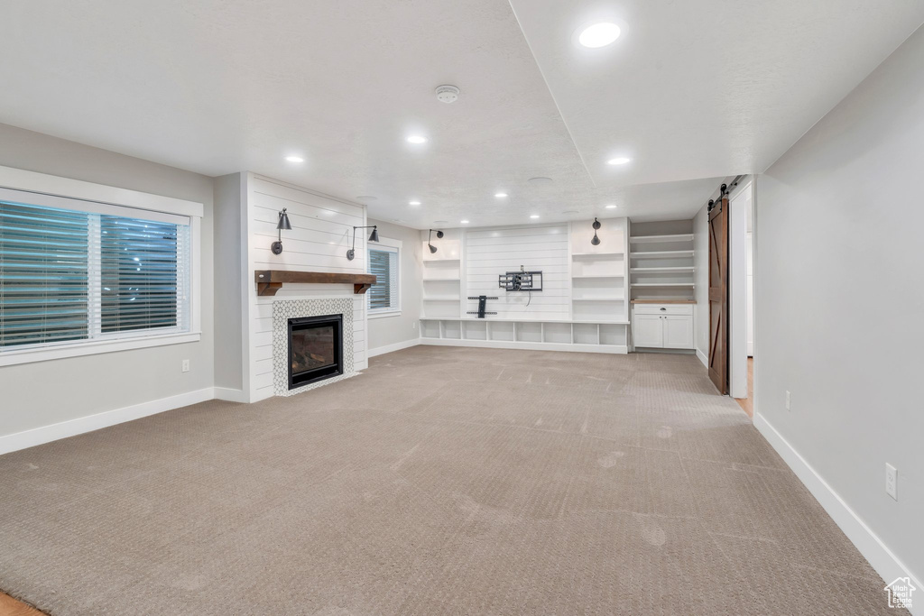 Unfurnished living room featuring light colored carpet, baseboards, recessed lighting, a barn door, and a fireplace