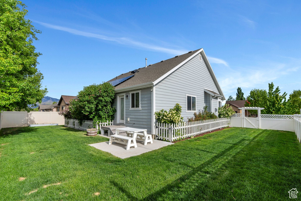 Rear view of house with a patio, roof mounted solar panels, and a shingled roof