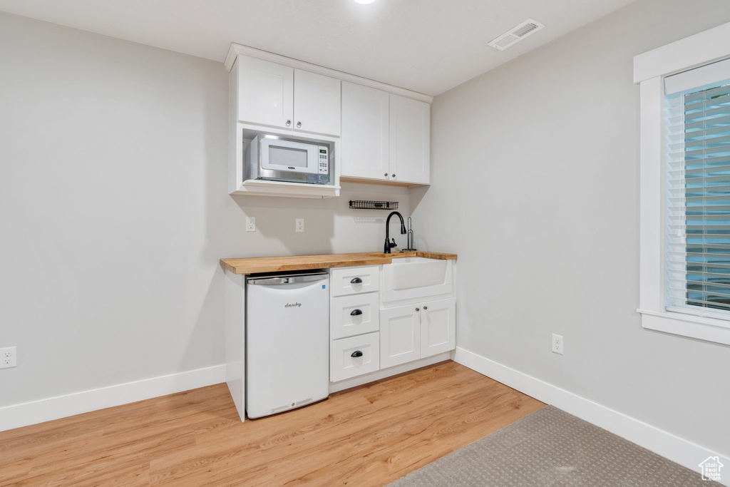 Kitchen with white appliances, a sink, butcher block countertops, light wood-style floors, and white cabinetry