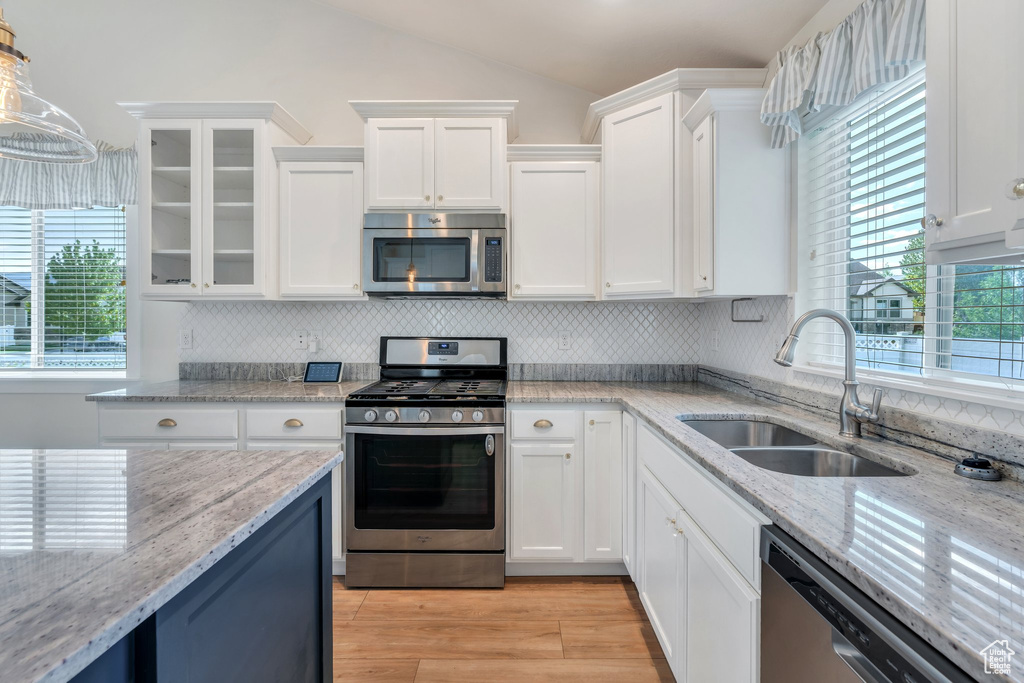 Kitchen featuring stainless steel appliances, a sink, white cabinets, decorative backsplash, and light wood finished floors