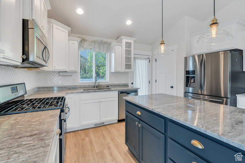 Kitchen with stainless steel appliances, a sink, white cabinets, blue cabinetry, and tasteful backsplash