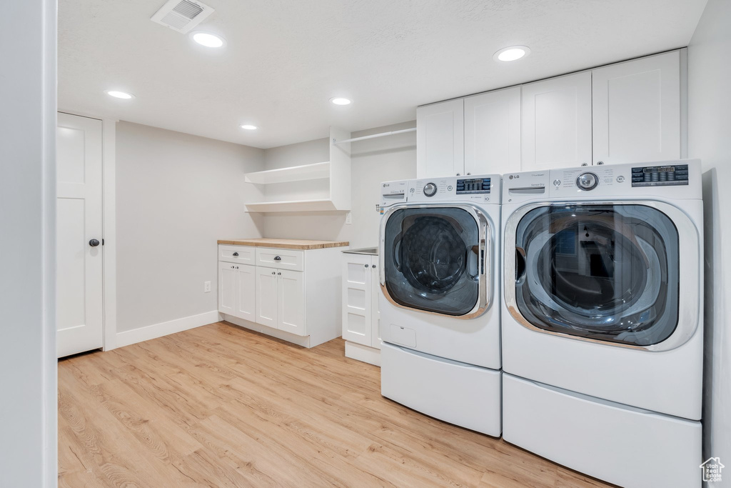 Laundry area with washing machine and dryer, light wood finished floors, baseboards, recessed lighting, and cabinet space