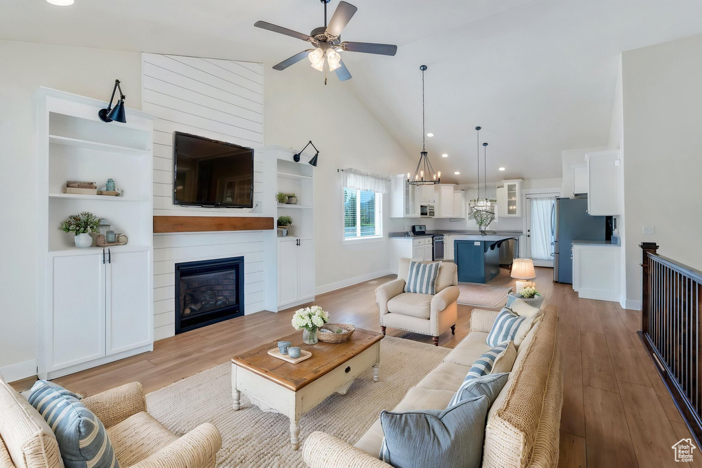 Living area with high vaulted ceiling, light wood-style floors, ceiling fan, a fireplace, and baseboards