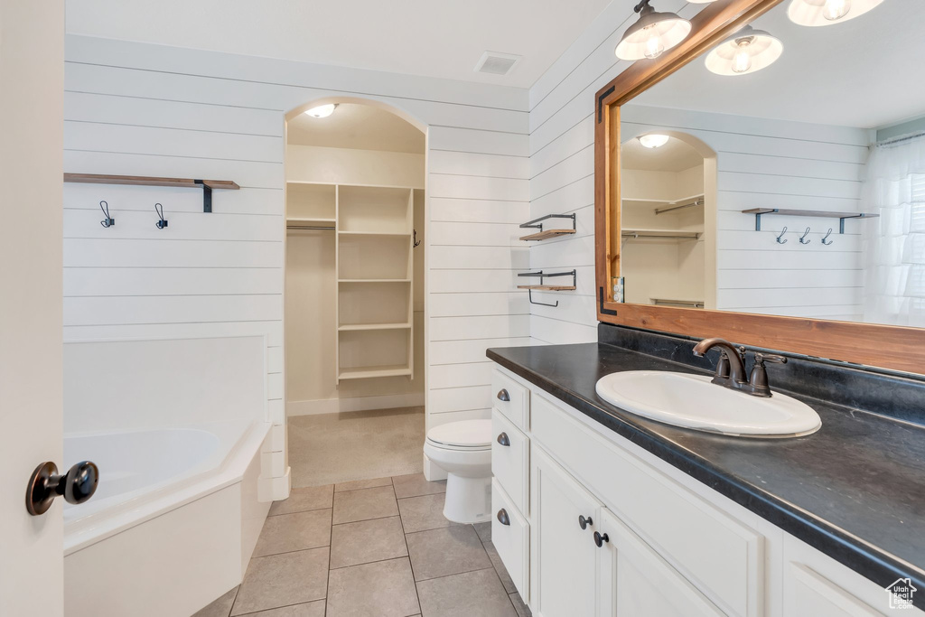 Bathroom with wood walls, tile patterned floors, a spacious closet, toilet, and vanity