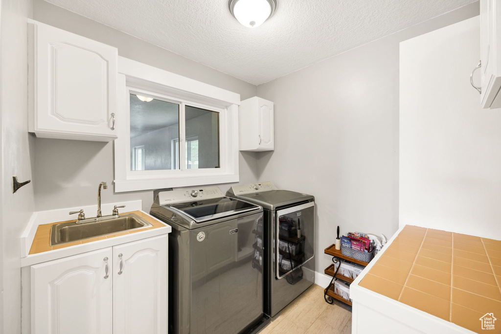 Laundry room featuring washer and clothes dryer, cabinet space, light wood finished floors, and a textured ceiling