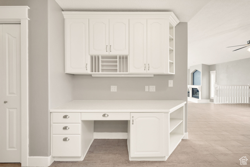 Unfurnished office with built in desk, a ceiling fan, and light wood-type flooring